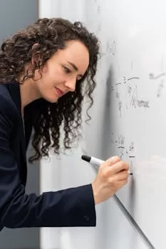 Female engineer solving equations on whiteboard with focus and precision.