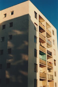 Mid-rise apartment building with balconies in warm daylight, casting soft shadows.