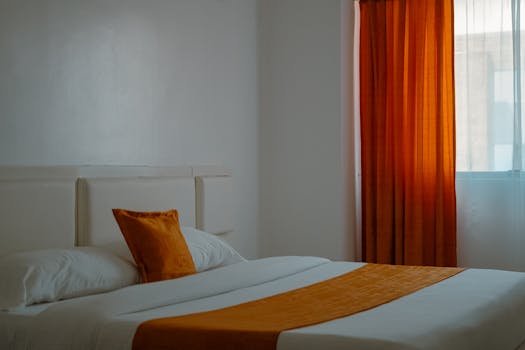 Gestión de Arrendamientos 9 Warm and inviting hotel room with orange curtains and bedding creating a cozy ambiance.